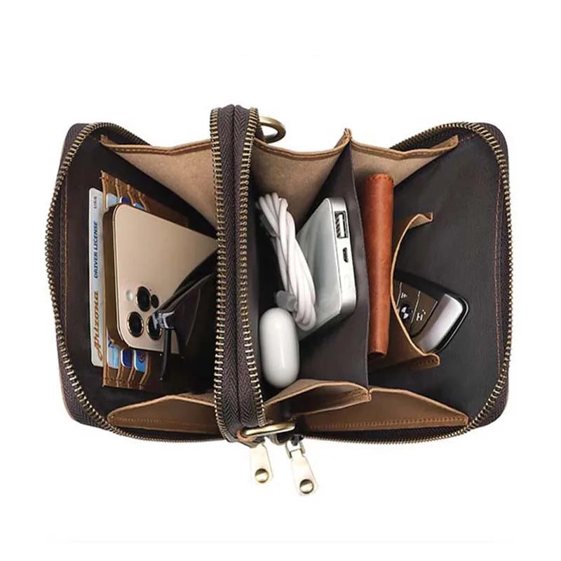 Portafoglio in pelle marrone aperto con scomparti, contenente smartphone, carte di credito, cavi e chiavi auto. Accessorio elegante e funzionale.