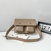 Borsa a tracolla beige con doppie tasche frontali, design minimalista, su sfondo grigio. Accessorio moda elegante per donna.