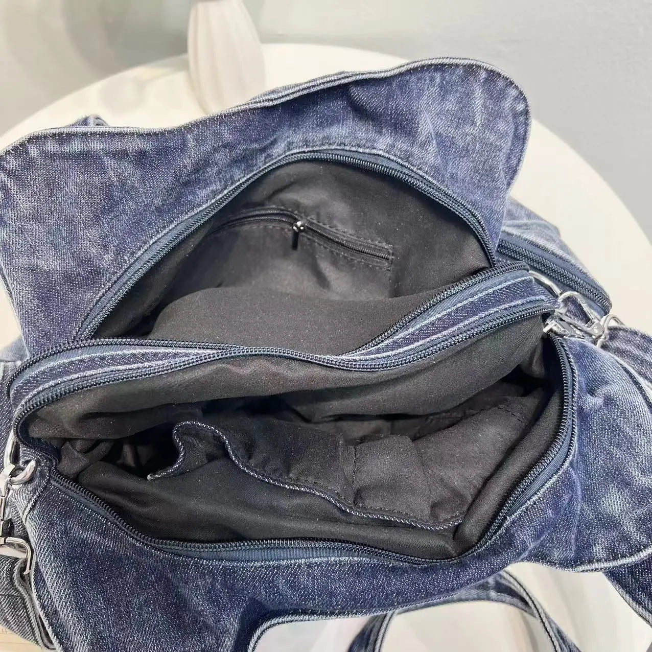 Borsa in denim blu aperta su tavolo bianco, con scomparti interni visibili. Design casual, ideale per moda quotidiana e accessori.