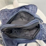 Borsa in denim blu aperta su tavolo bianco, con scomparti interni visibili. Design casual, ideale per moda quotidiana e accessori.