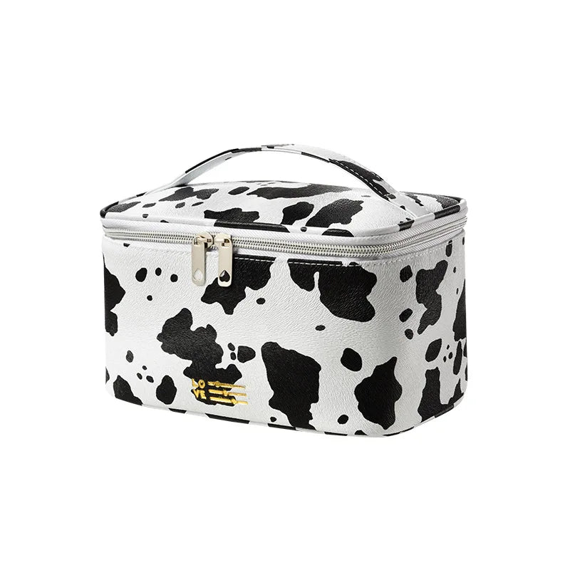 Astuccio cosmetico in ecopelle con stampa mucca bianco e nero, chiusura a zip, manico superiore. Design elegante e pratico per viaggi e organizzazione.