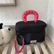 Borsa nera con manico rosa numerato, design moderno, su scaffale in legno. Accessorio moda, stile unico, perfetto per uso quotidiano.