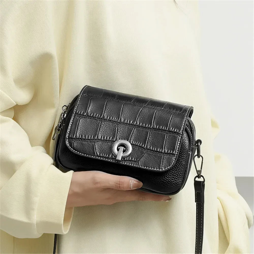 Borsa a tracolla nera in pelle con motivo coccodrillo, chiusura a girello, indossata da una persona. Accessorio moda elegante e versatile.