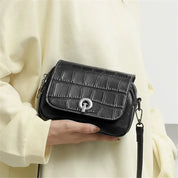 Borsa a tracolla nera in pelle con motivo coccodrillo, chiusura a girello, indossata da una persona. Accessorio moda elegante e versatile.
