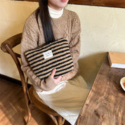 Donna seduta con maglione beige e borsa a righe nere e beige su sedia di legno. Moda autunnale, accessori invernali, stile casual chic.