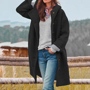 Donna con cappotto nero invernale, maglione grigio e jeans, all'aperto. Moda autunno inverno, abbigliamento casual elegante, paesaggio naturale.