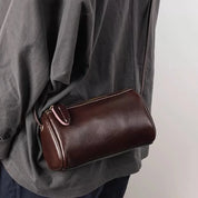 Borsa a tracolla in pelle marrone scuro, design compatto e moderno, indossata su abbigliamento casual. Accessorio moda elegante e versatile.