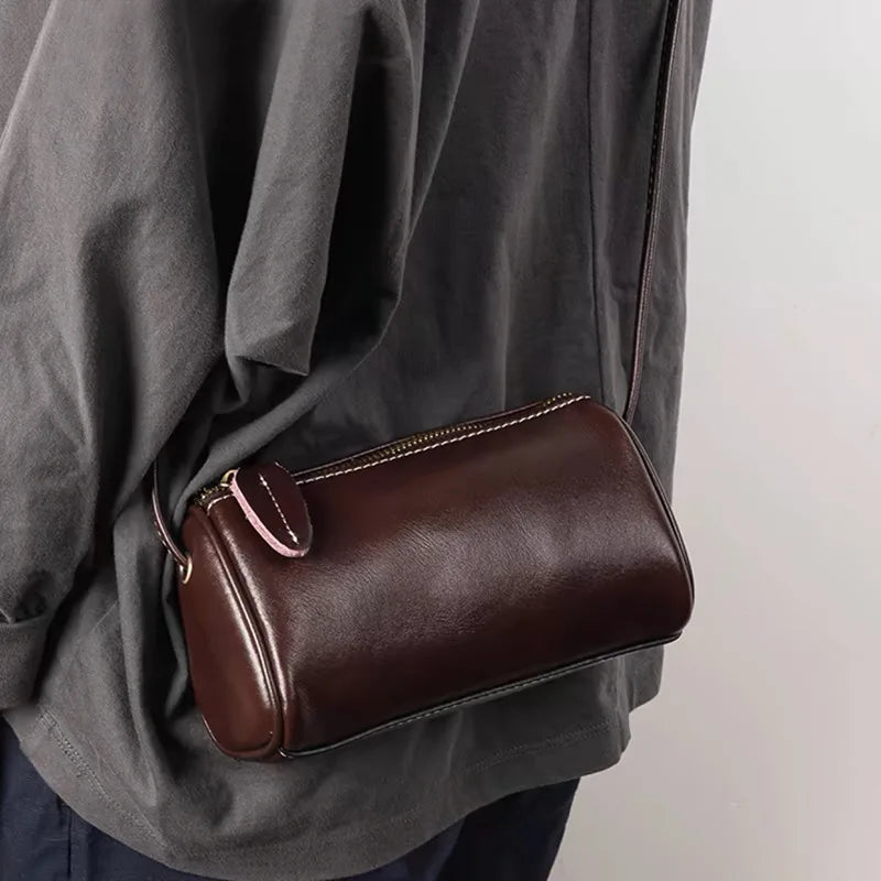 Borsa a tracolla in pelle marrone scuro, design compatto e moderno, indossata su abbigliamento casual. Accessorio moda elegante e versatile.