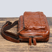 Borsa a tracolla in pelle marrone vintage su tavolo di legno, con cerniere robuste e tracolla regolabile. Accessorio moda uomo elegante e pratico.