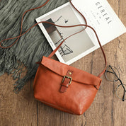 Borsa a tracolla in pelle marrone su tavolo di legno, con occhiali e rivista. Elegante accessorio moda donna, stile vintage, alta qualità.