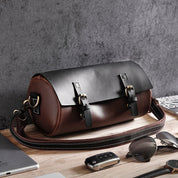 Borsa a tracolla in pelle marrone e nera su tavolo di legno, con fibbie metalliche. Accessorio moda elegante per uomo, ideale per viaggi e lavoro.