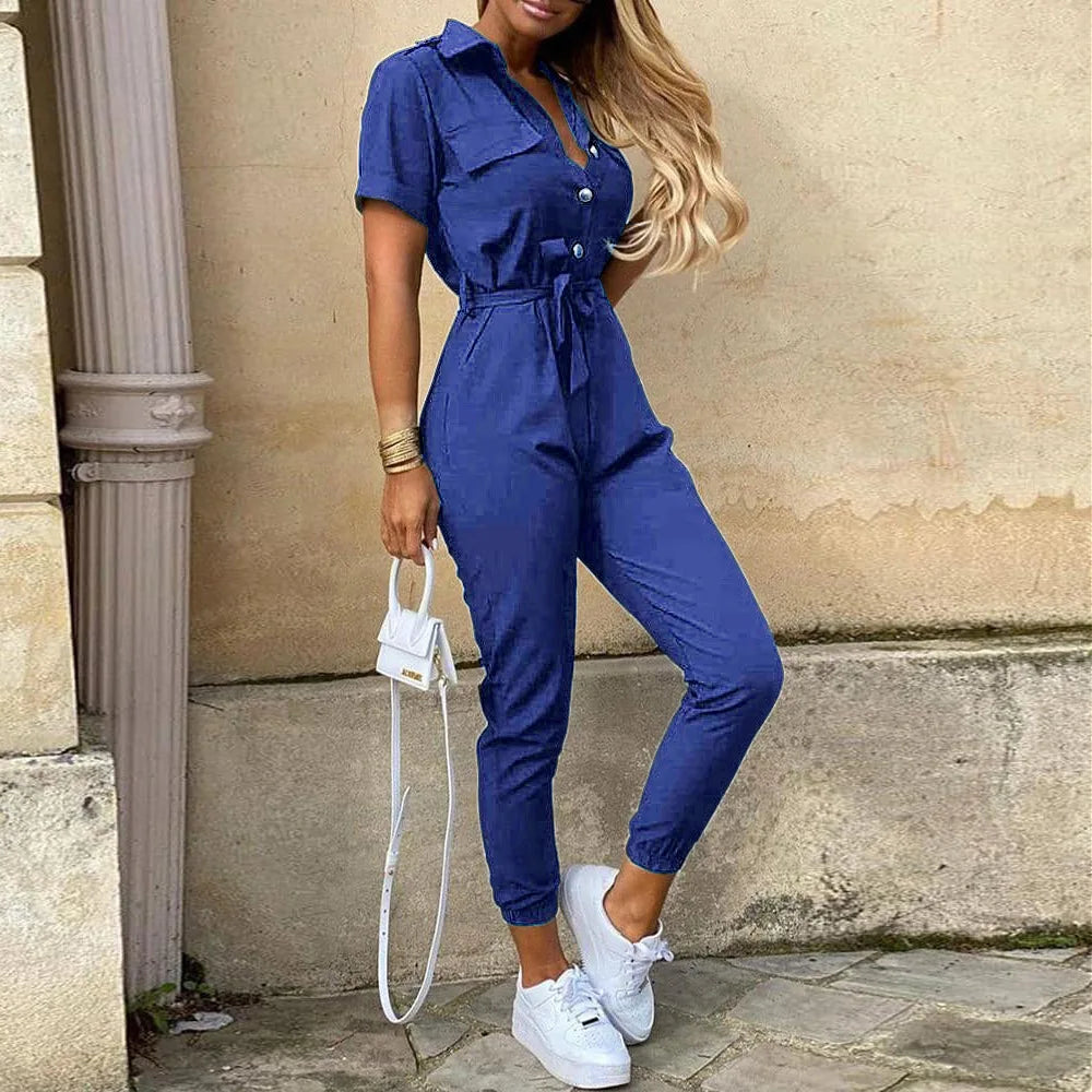 Tuta jumpsuit blu donna, maniche corte, cintura in vita, abbinata a sneakers bianche e borsa piccola. Look casual elegante per moda estiva.