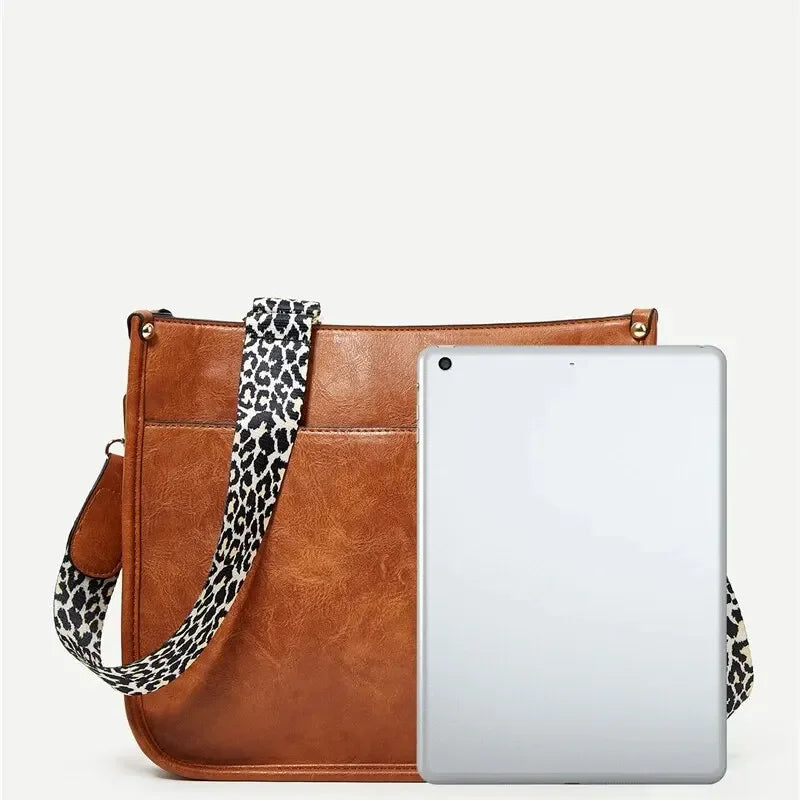 Borsa a tracolla in pelle marrone con cinturino leopardato, affiancata da un tablet grigio. Accessorio moda donna, elegante e pratico.