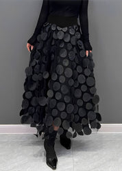Gonna lunga nera con cerchi decorativi, indossata con top nero a maniche lunghe e stivali a punta. Moda elegante, abbigliamento femminile chic.