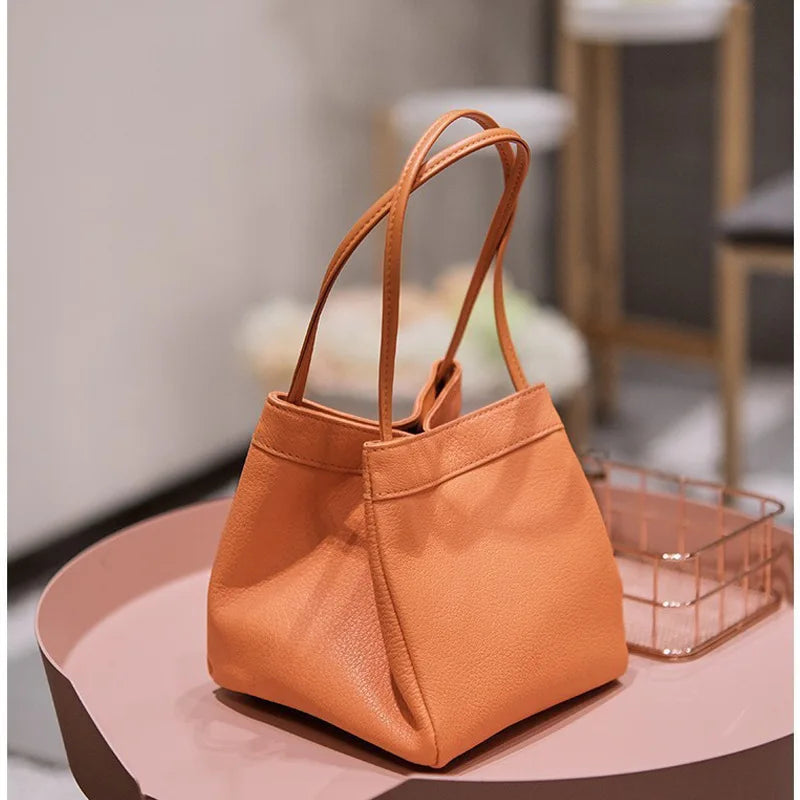 Borsa a mano in pelle arancione su tavolo rosa, design elegante e moderno, perfetta per moda femminile, accessorio di tendenza 2023.