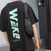 Maglietta nera con scritta "CHARMA" e borsa a tracolla nera. Design casual, moda urbana, abbigliamento streetwear uomo.