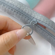 Mano che apre una cerniera grigia su una borsa trasparente. Accessorio moda, borsa organizer, chiusura lampo resistente.