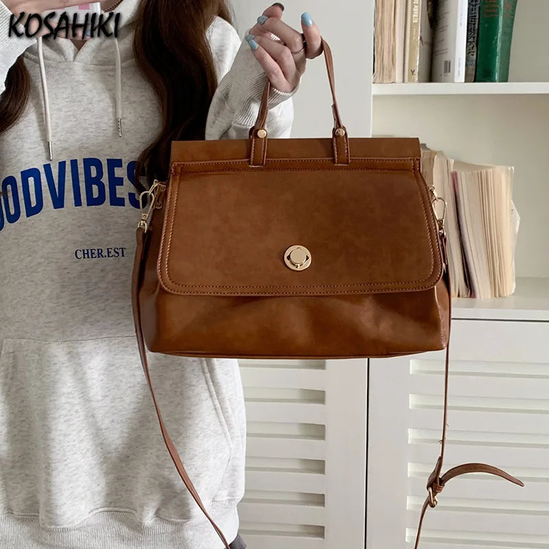 Borsa a mano in pelle marrone con tracolla regolabile, indossata da una donna in felpa grigia. Design elegante, ideale per moda casual e shopping.