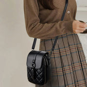 Borsa a tracolla nera trapuntata in pelle, indossata da donna con maglione marrone e gonna a quadri. Accessorio moda elegante e versatile.