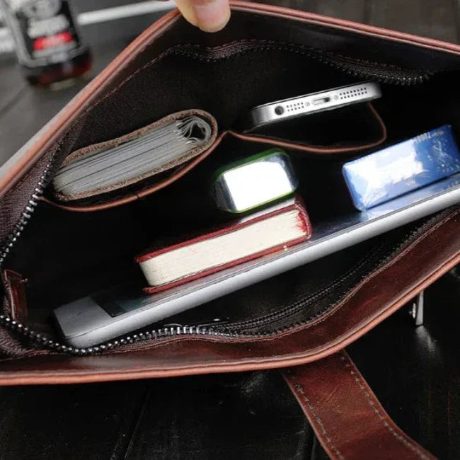 Interno di una borsa in pelle marrone con smartphone, portafoglio, libro e pacchetto di fazzoletti. Accessori moda, organizzazione, eleganza.