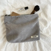Astuccio cosmetico grigio Sozakka su tessuto bianco, contenente pennello trucco, flacone profumo, specchio e crema. Accessori bellezza essenziali.
