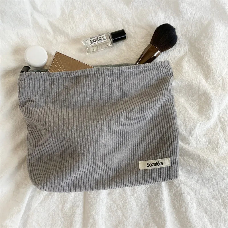 Astuccio cosmetico grigio Sozakka su tessuto bianco, contenente pennello trucco, flacone profumo, specchio e crema. Accessori bellezza essenziali.