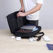 Zaino nero aperto su tavolo, con libri, quaderni e accessori tecnologici. Uomo in maglietta bianca. Accessori: smartphone, mouse, auricolari.
