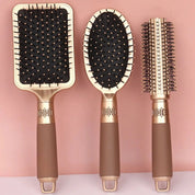 Set di tre spazzole per capelli dorate su sfondo rosa: spazzola piatta, ovale e rotonda. Accessori styling eleganti e funzionali per capelli.