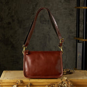 Borsa a tracolla in pelle marrone su sfondo rustico, design elegante con fibbie dorate. Accessorio moda donna, stile vintage.