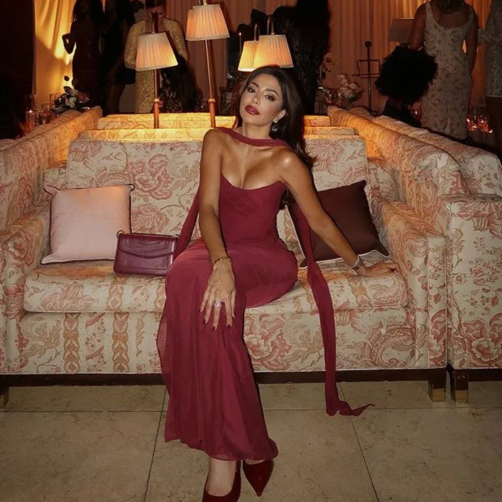Donna in abito rosso elegante seduta su divano decorato, ambiente lussuoso con lampade soffuse, atmosfera serale raffinata.