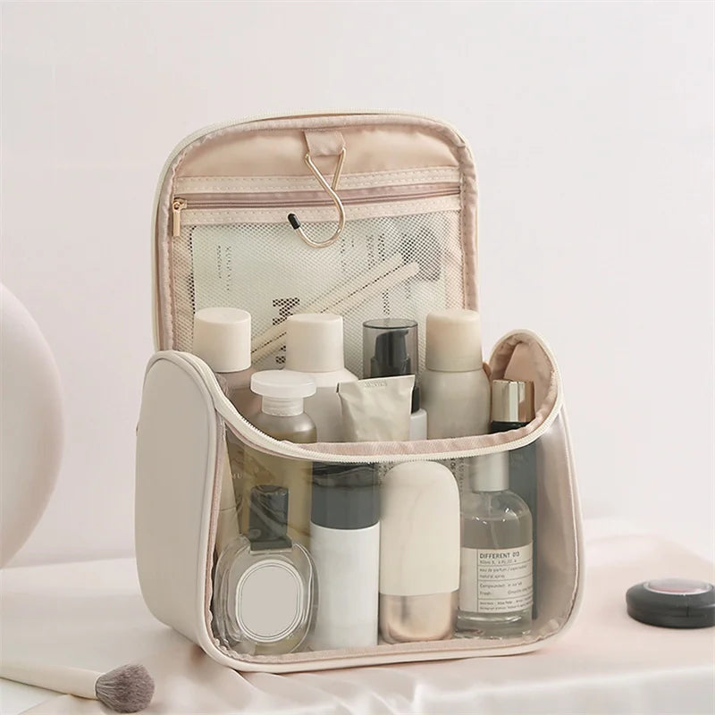 Borsa da toilette trasparente con prodotti cosmetici, pennello trucco e gancio dorato. Ideale per organizzare articoli da viaggio e bellezza.