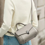 Donna con maglione bianco indossa borsa a tracolla grigia in pelle, design elegante e moderno, accessorio moda femminile, strada cittadina.