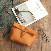 Borsa a tracolla in pelle marrone su tavolo di legno, accanto a rivista e occhiali. Accessorio moda elegante, perfetto per look casual e chic.
