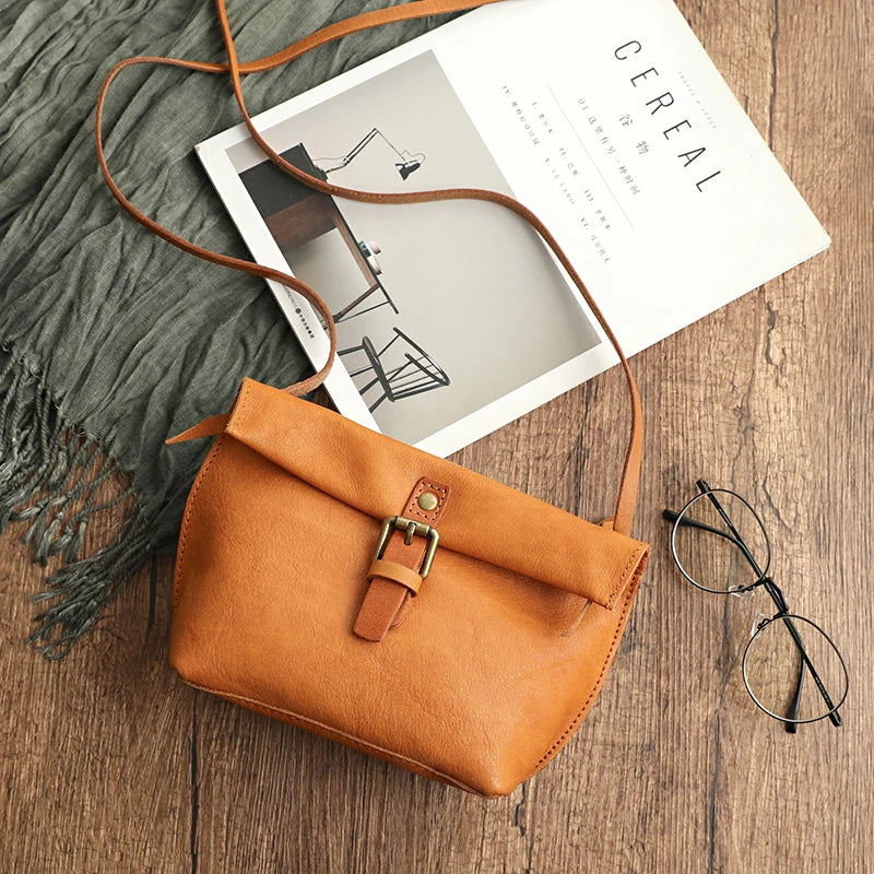 Borsa a tracolla in pelle marrone su tavolo di legno, accanto a rivista e occhiali. Accessorio moda elegante, perfetto per look casual e chic.