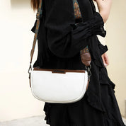 Borsa a tracolla bianca con dettagli marroni, cinturino regolabile decorato, indossata da una persona in abito nero. Accessorio moda elegante.