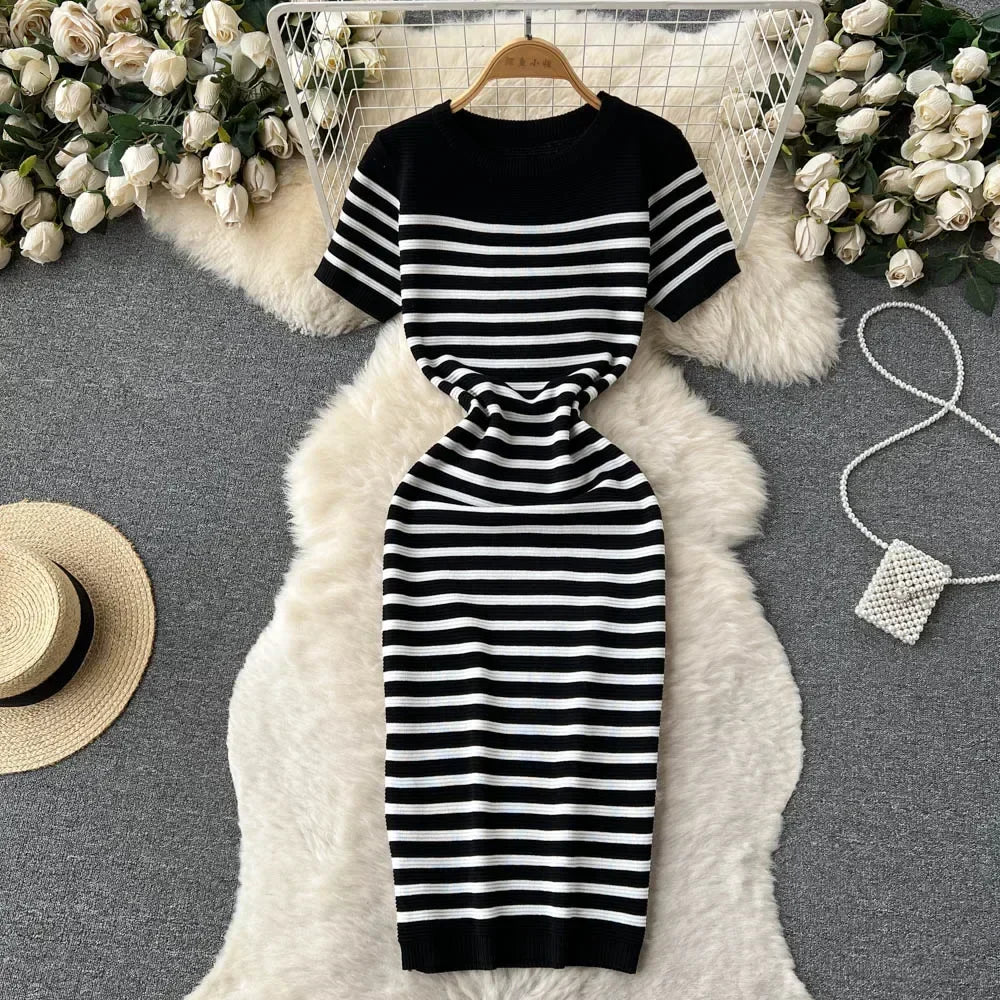 Abito a righe bianche e nere su tappeto bianco, circondato da fiori bianchi e cappello di paglia. Elegante, casual, moda donna, stile estivo.