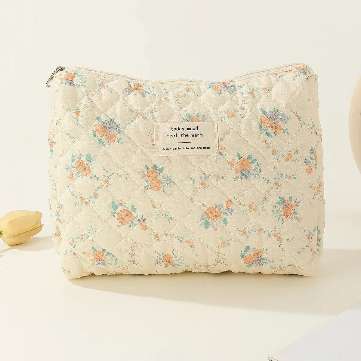 Borsa cosmetica trapuntata in cotone floreale, beige con fiori arancioni e blu, chiusura a zip, ideale per trucco e accessori da viaggio.