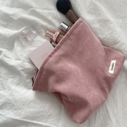 Astuccio cosmetico rosa in tessuto a coste su letto bianco, contenente trucchi e pennelli. Accessorio moda, organizzazione trucco, stile elegante.