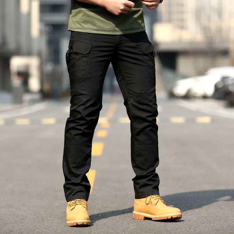Pantaloni cargo neri da uomo, tasche multiple, indossati con scarpe gialle su strada urbana. Stile casual, moda maschile, abbigliamento outdoor.