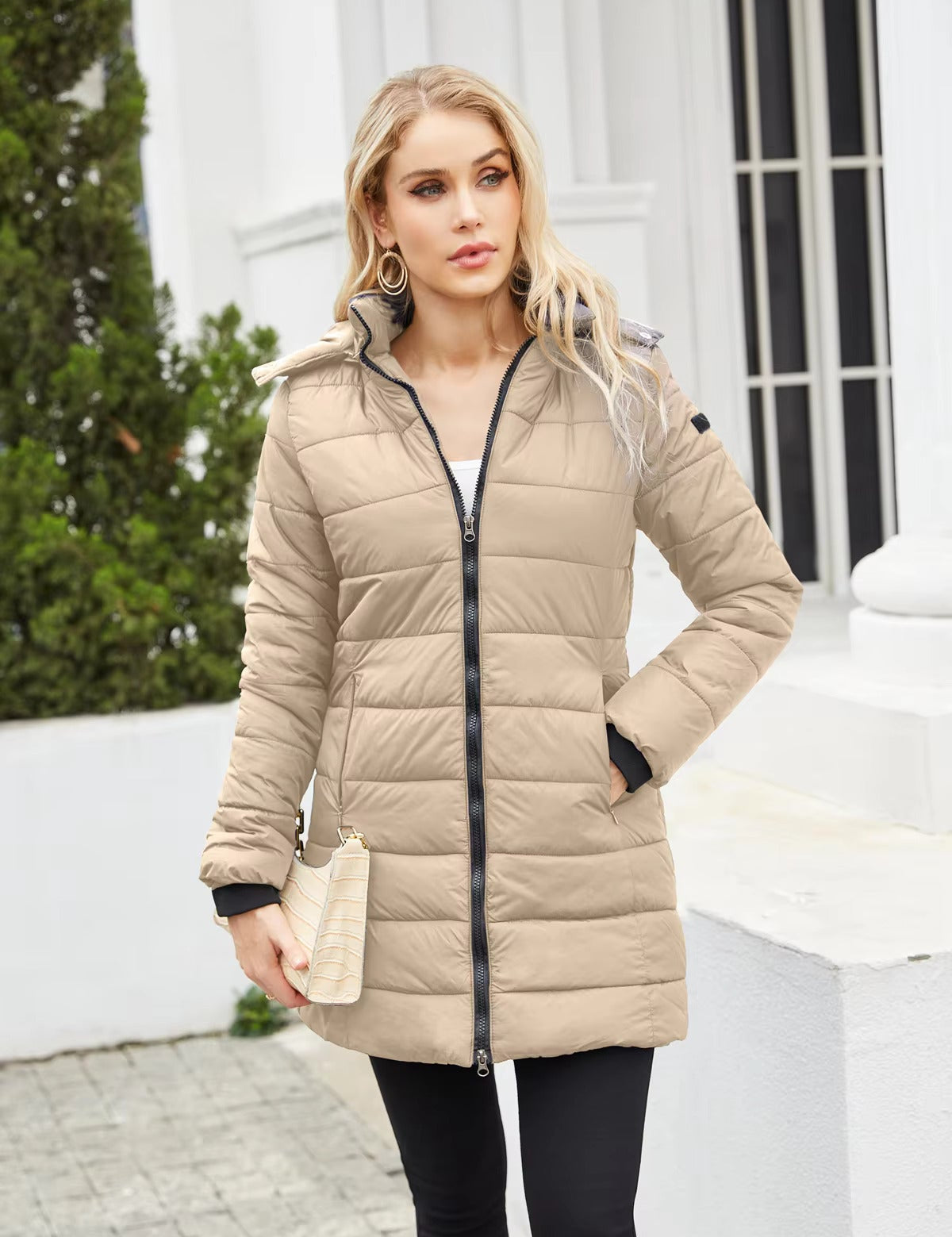 Donna con cappotto imbottito beige, zip frontale, tasche laterali, sfondo urbano. Moda invernale, abbigliamento caldo, stile casual elegante.