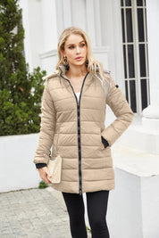 Donna con cappotto imbottito beige, zip frontale, tasche laterali, sfondo urbano. Moda invernale, abbigliamento caldo, stile casual elegante.