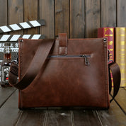 Borsa a tracolla in pelle marrone con zip, design elegante, ideale per lavoro e viaggio. Sfondo con libri e bottiglia. Accessorio moda uomo.