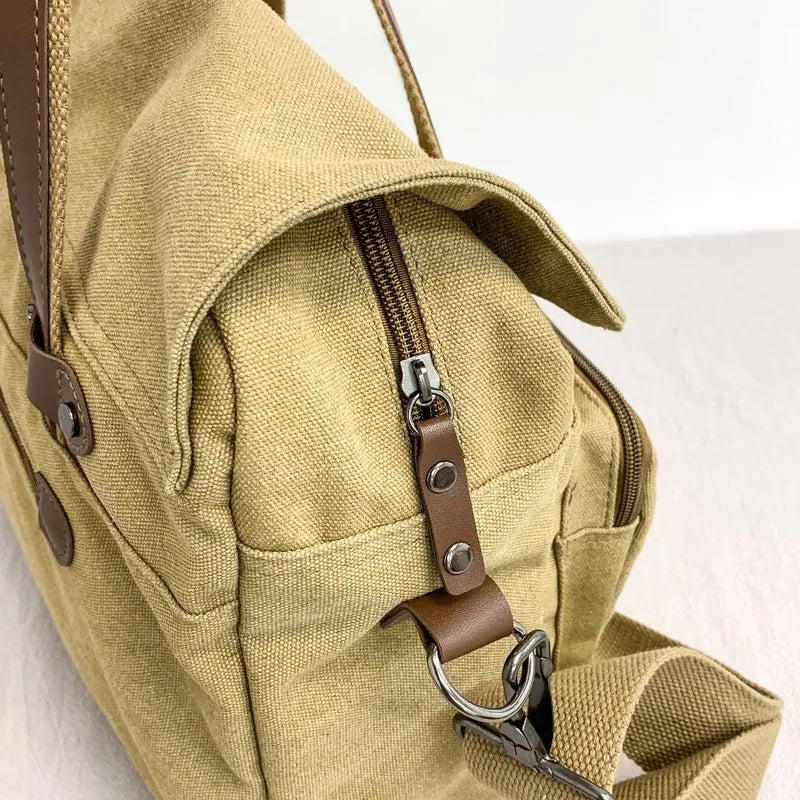 Borsa a tracolla in tela beige con cerniera e dettagli in pelle marrone, design casual, ideale per viaggi e uso quotidiano.