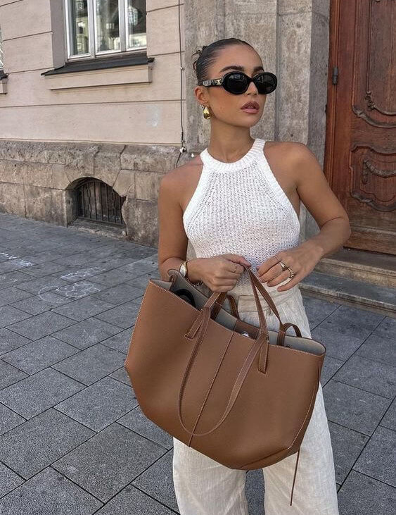 Donna elegante con occhiali da sole, top bianco e borsa in pelle marrone su strada cittadina. Moda estiva, accessori di tendenza, look casual chic.