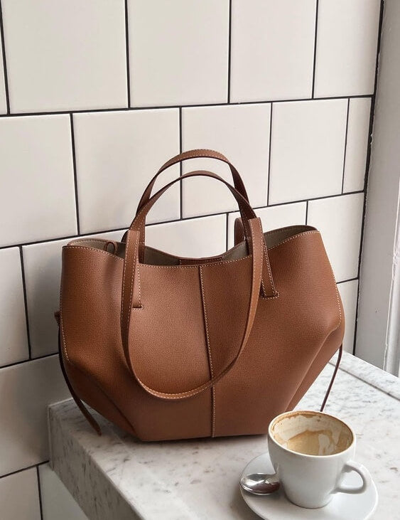 Borsa a mano in pelle marrone su tavolo di marmo bianco, accanto a tazza di caffè. Elegante accessorio moda donna, design moderno e raffinato.