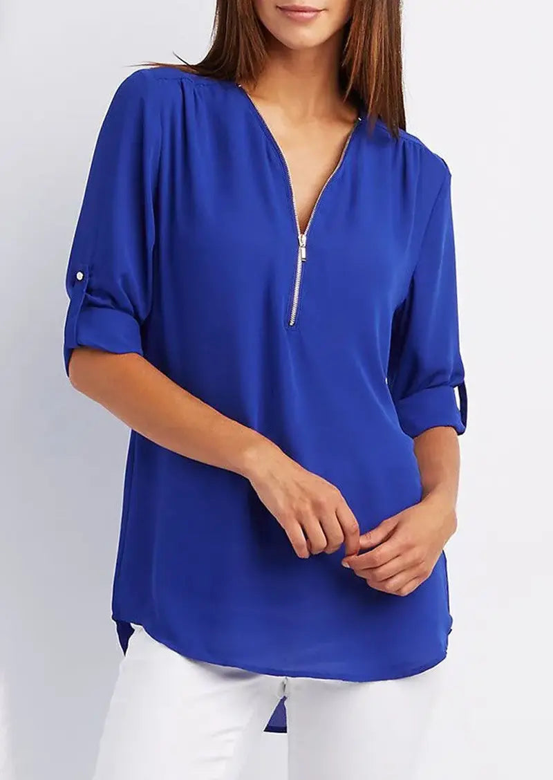 Donna con blusa blu elettrico a maniche lunghe, scollo a V con zip, abbinata a pantaloni bianchi. Moda casual elegante, abbigliamento femminile.