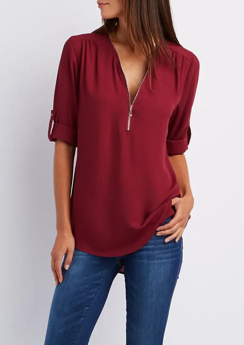 Blusa bordeaux con zip frontale, maniche a 3/4 arrotolate, indossata con jeans blu. Elegante e casual, perfetta per moda femminile autunnale.