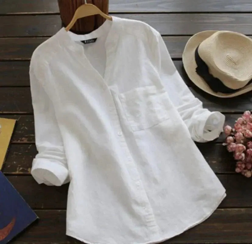 Camicia bianca in lino da uomo su appendiabiti, maniche lunghe, colletto alla coreana, stile casual. Sfondo con cappello di paglia e fiori.