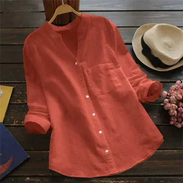 Camicia di lino arancione a maniche lunghe su sfondo di legno, con cappello di paglia e fiori. Moda casual donna, abbigliamento estivo elegante.