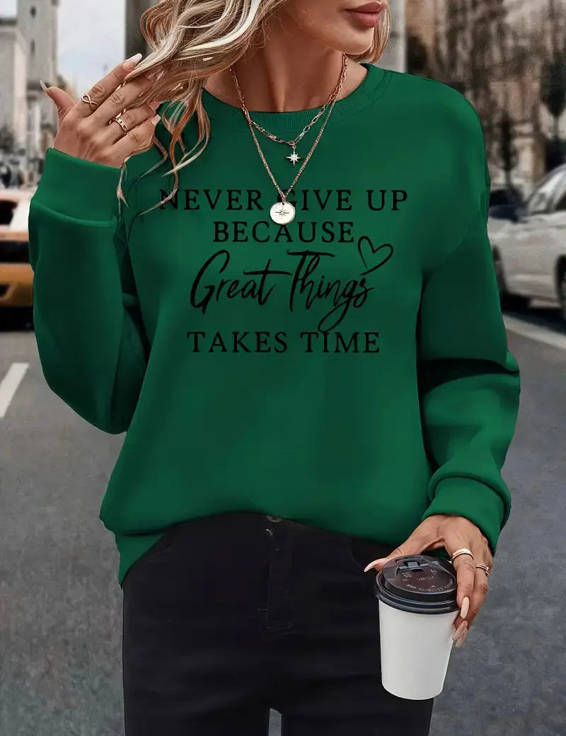 Donna con maglione verde con scritta motivazionale, collane dorate, pantaloni neri, tiene una tazza da caffè. Moda casual autunnale urbana.